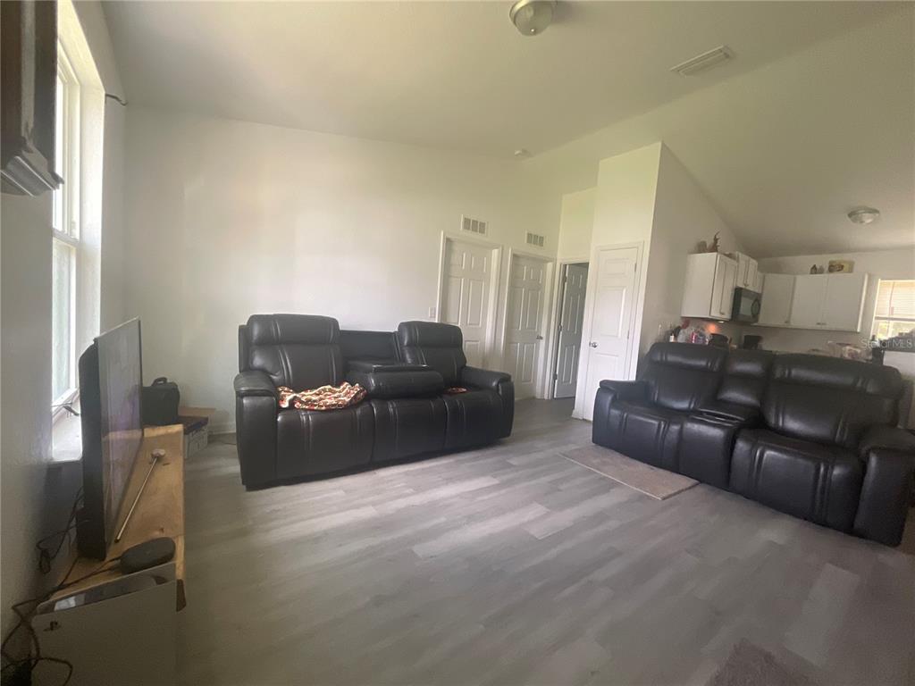 A living room with two black leather reclining sofas, light wood-look flooring, and white walls — 15309 SW 52ND CIRCLE, OCALA, FL