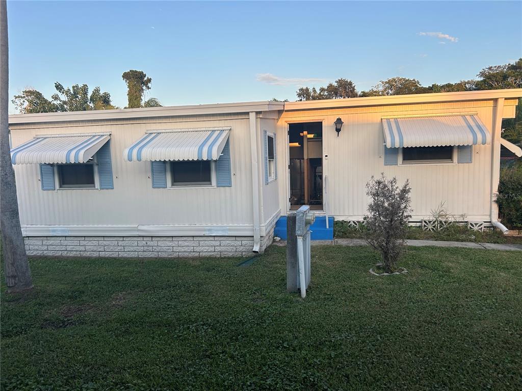 A single-story mobile home with white siding, blue-striped window awnings, and a small front entrance — 4432 TUCKER SQUARE, NEW PORT RICHEY, FL