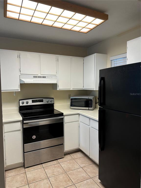 A kitchen features white cabinets, stainless steel appliances, a black refrigerator, and tile flooring — 83 SE 16TH AVENUE UNIT E102, GAINESVILLE, FL