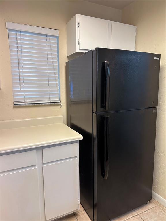 A black refrigerator stands next to white cabinets and a window with blinds — 83 SE 16TH AVENUE UNIT E102, GAINESVILLE, FL