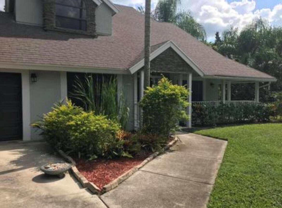 A view of a house exterior featuring a concrete walkway, landscaping, and a stone-accented entryway — 11852 61st Street N, FL 33412, FL