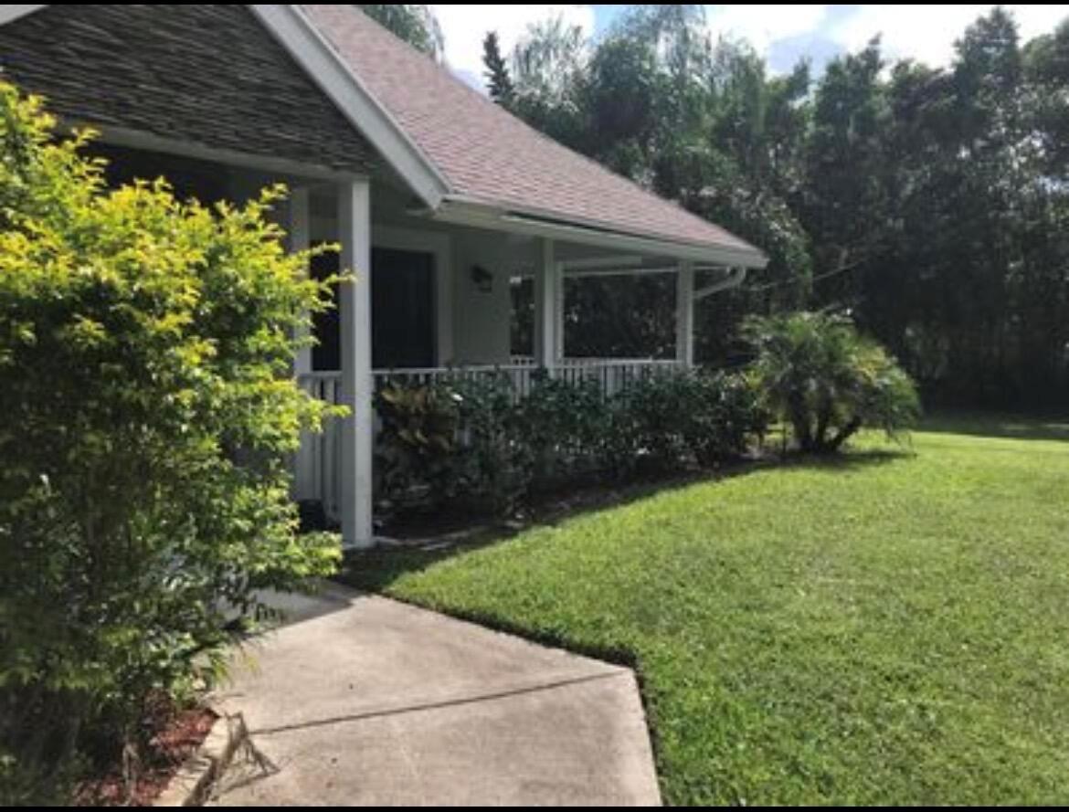 A concrete walkway leads to the covered porch of a house with a shingled roof — 11852 61st Street N, FL 33412, FL
