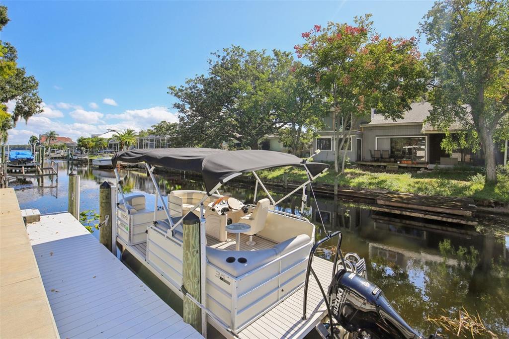 A pontoon boat is docked at a wooden pier on a canal beside a house — 3140 N CANAL DRIVE, PALM HARBOR, FL