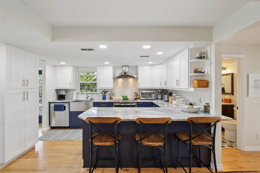 A kitchen features white upper cabinets, navy lower cabinets, a marble countertop, and three barstools — 3140 N CANAL DRIVE, PALM HARBOR, FL
