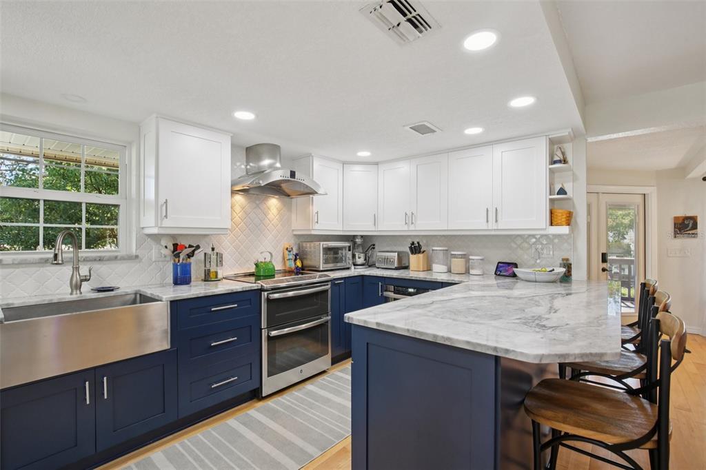 A kitchen features blue lower cabinets, white upper cabinets, a farmhouse sink, and marble countertops — 3140 N CANAL DRIVE, PALM HARBOR, FL