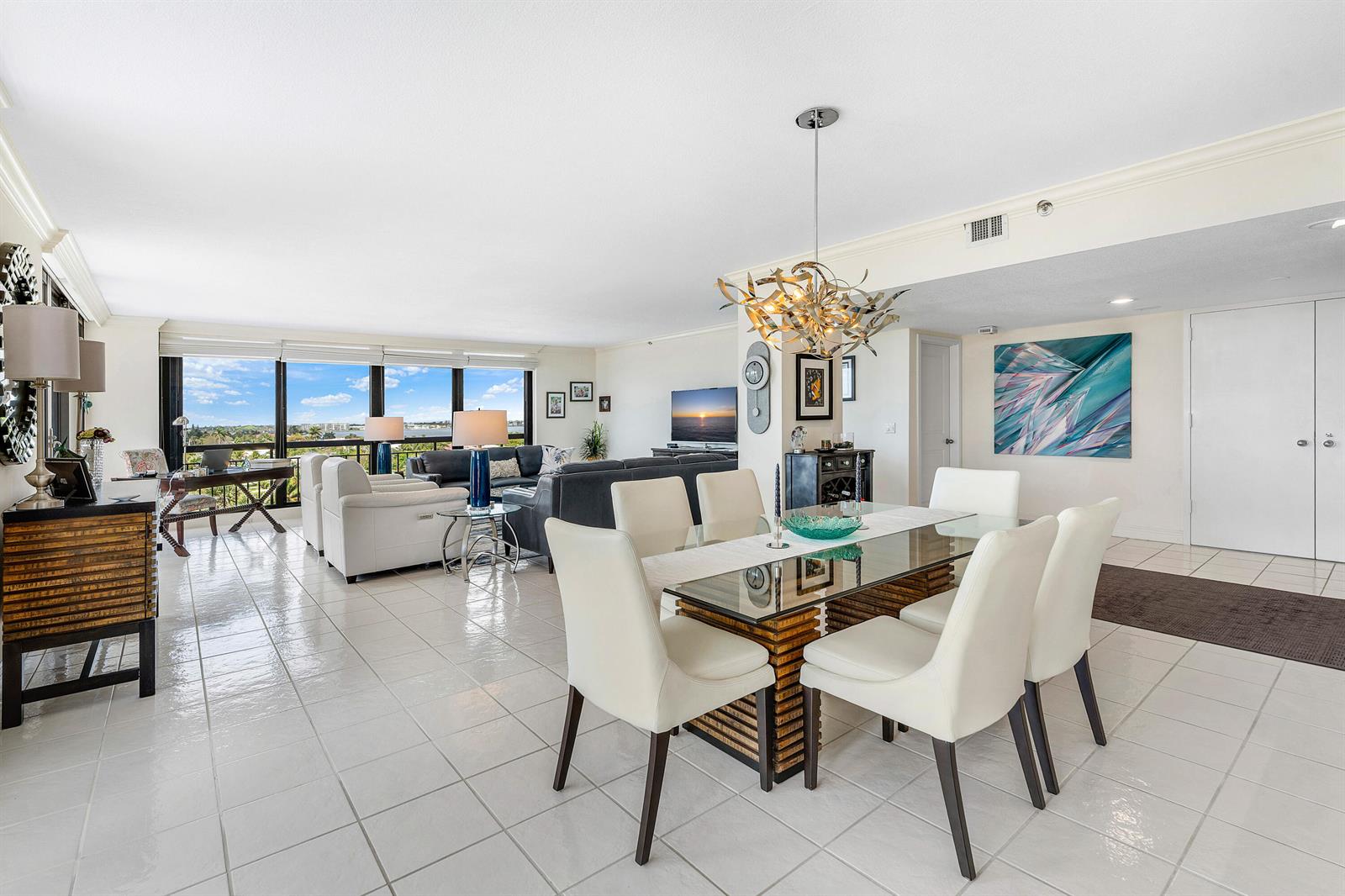 An open-concept living and dining area features white tile floors, a glass-topped table, and windows — 4100 N Ocean Drive # 504, Singer Island FL 33404, SINGER ISLAND, FL