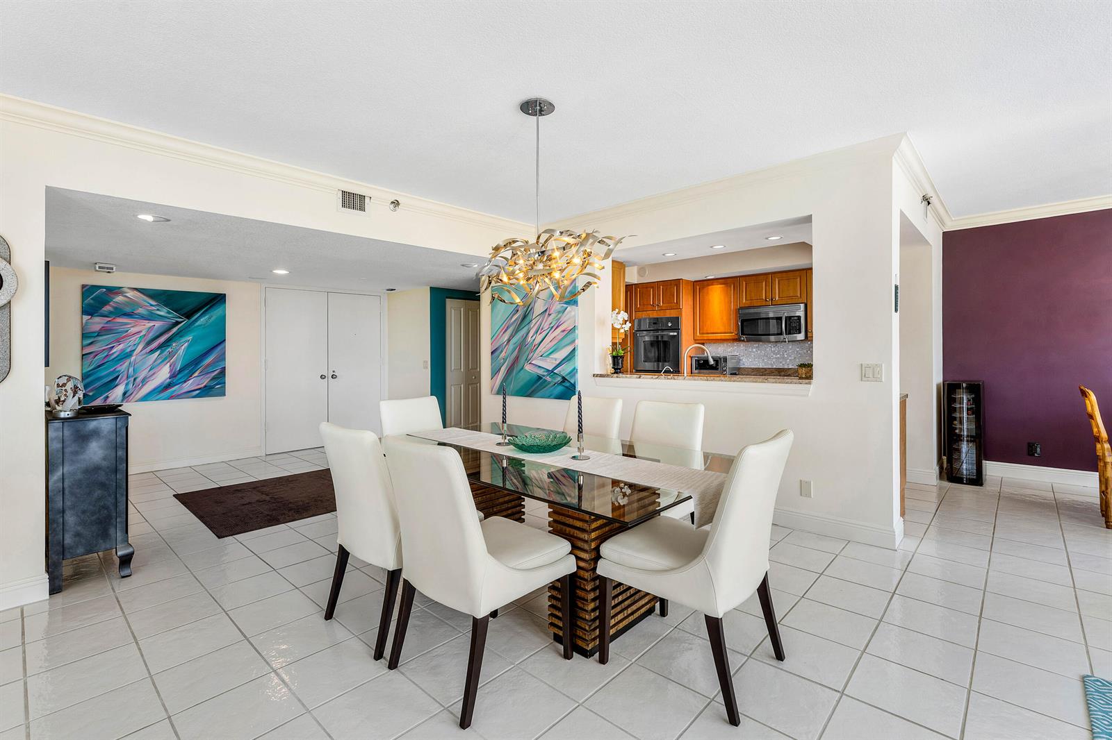 A dining room features a glass-topped table, white chairs, and a modern gold chandelier — 4100 N Ocean Drive # 504, Singer Island FL 33404, SINGER ISLAND, FL