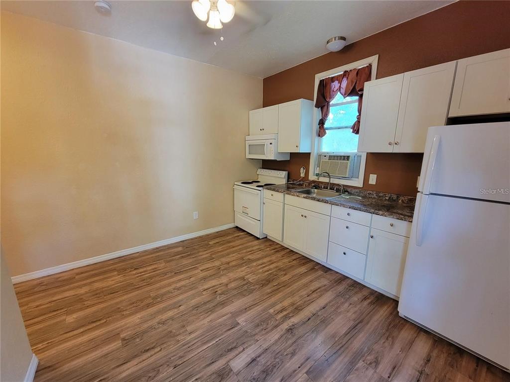 A kitchen features white cabinets, a white stove, a white refrigerator, and wood-look flooring — 965 NE 2ND STREET UNIT 4, OCALA, FL