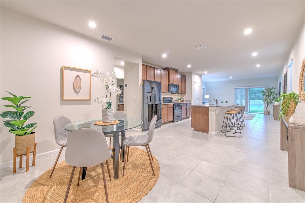 An open-concept kitchen and dining area features tile flooring, wood cabinetry, and a glass table — 11836 BRISTOL BRIDGE ROAD, SPRING HILL, FL