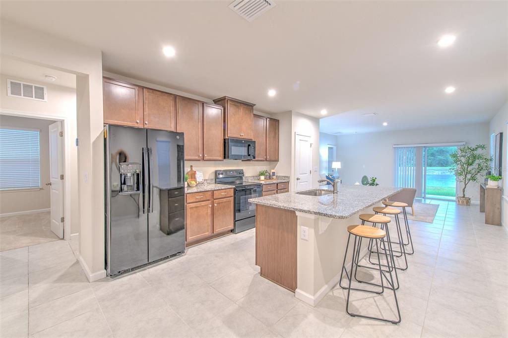 A kitchen with wood cabinets, granite countertops, stainless steel appliances, and a breakfast bar island — 11836 BRISTOL BRIDGE ROAD, SPRING HILL, FL