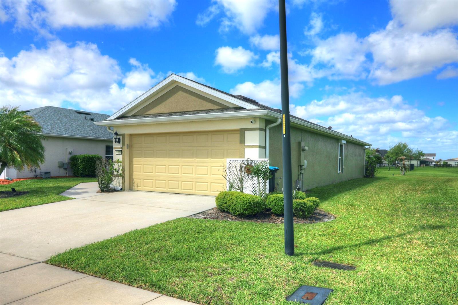 A tan single-story house with a two-car garage and a green lawn under a blue sky — 1420 Dittmer Circle SE, Palm Bay FL 32909, PALM BAY, FL