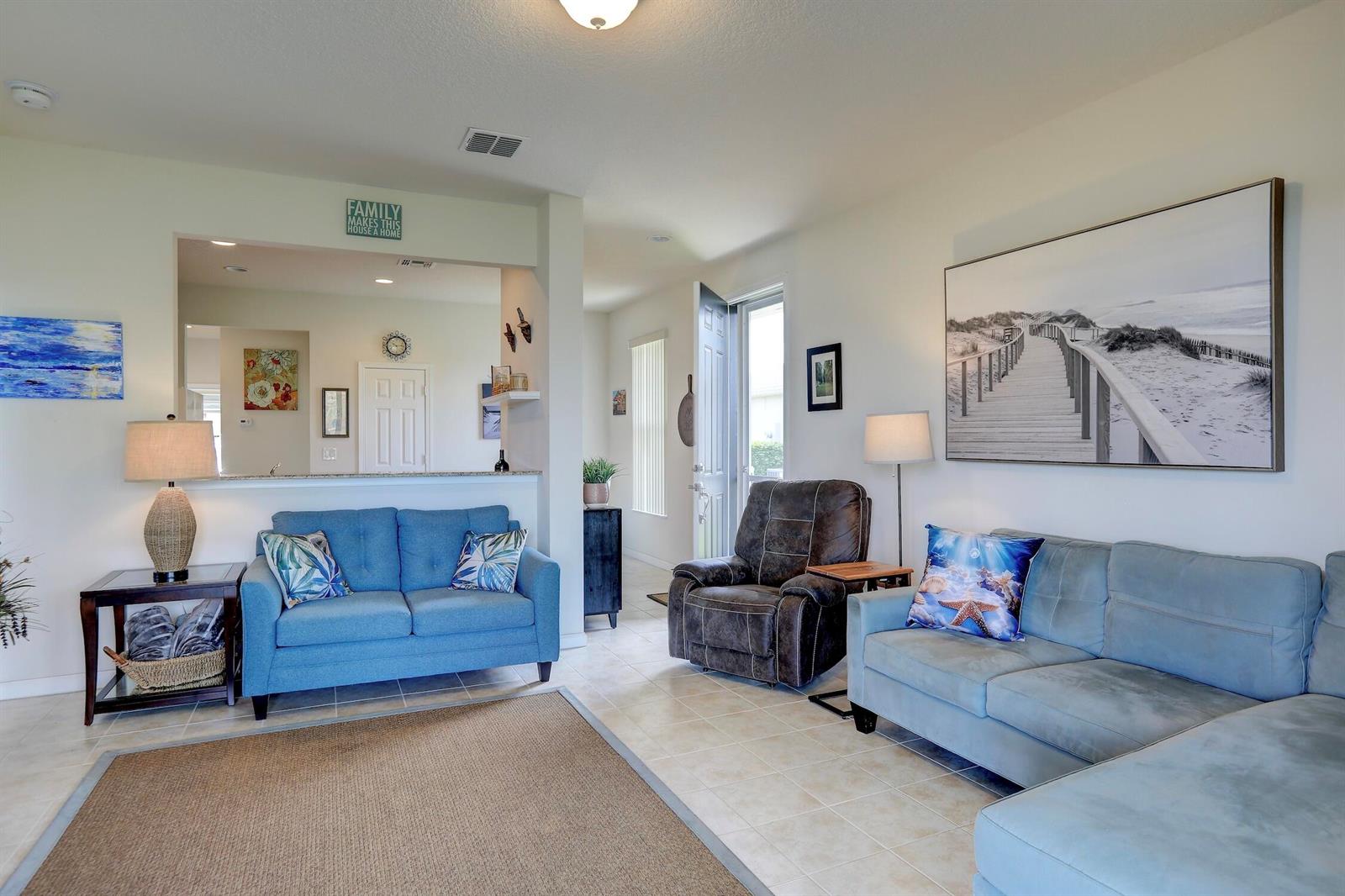 A living room features two blue sofas, a brown recliner, and a large beach-themed wall art — 1420 Dittmer Circle SE, Palm Bay FL 32909, PALM BAY, FL