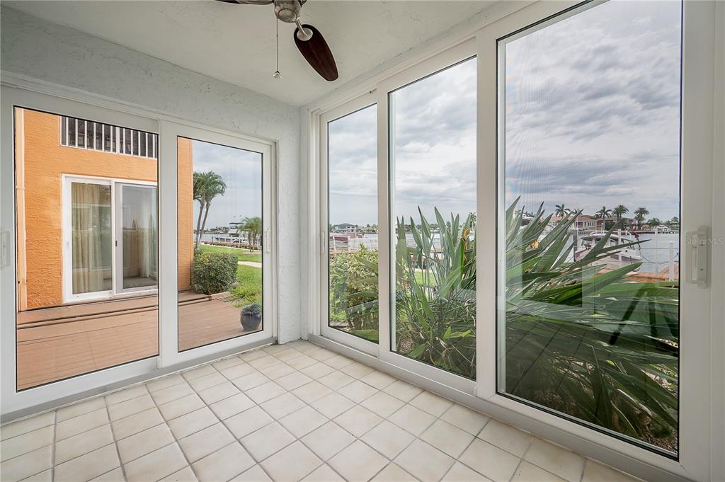 A sunroom with white tile flooring and large windows overlooking a canal with boats — 8921 BLIND PASS ROAD UNIT 143, ST PETE BEACH, FL