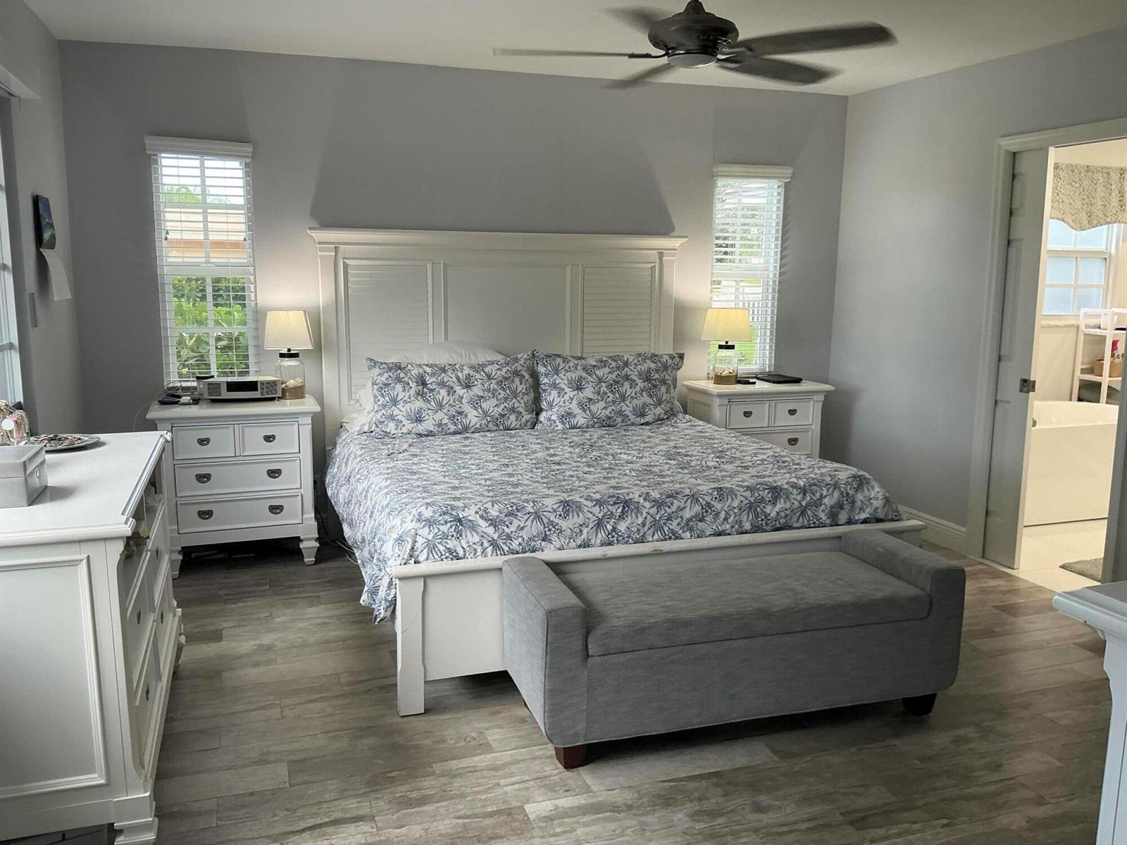 A bedroom features a white bed frame, matching nightstands, a gray bench, and light wood flooring — 18 Holly Drive, Boynton Beach FL 33436, BOYNTON BEACH, FL