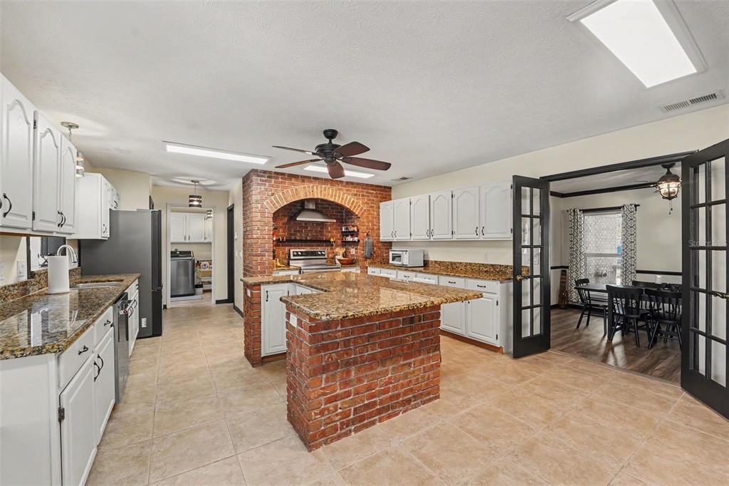 A kitchen features white cabinets, granite countertops, and a central brick island with an arch — 717 CAMROSE DRIVE, BRANDON, FL