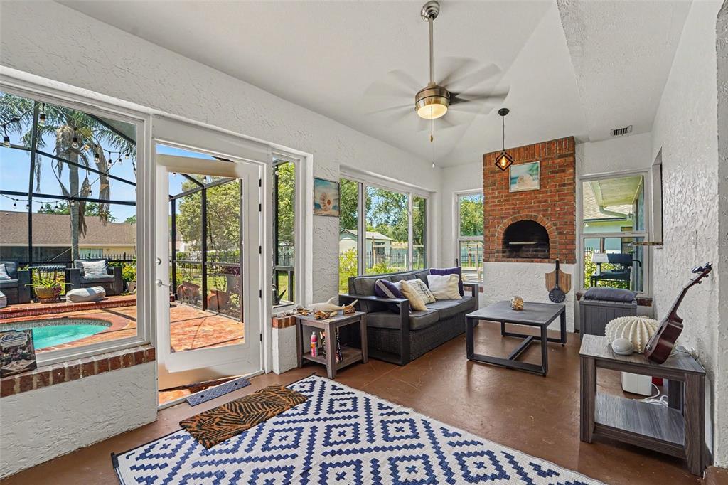 A sunroom features a brick fireplace, a ceiling fan, and a view of a pool — 717 CAMROSE DRIVE, BRANDON, FL