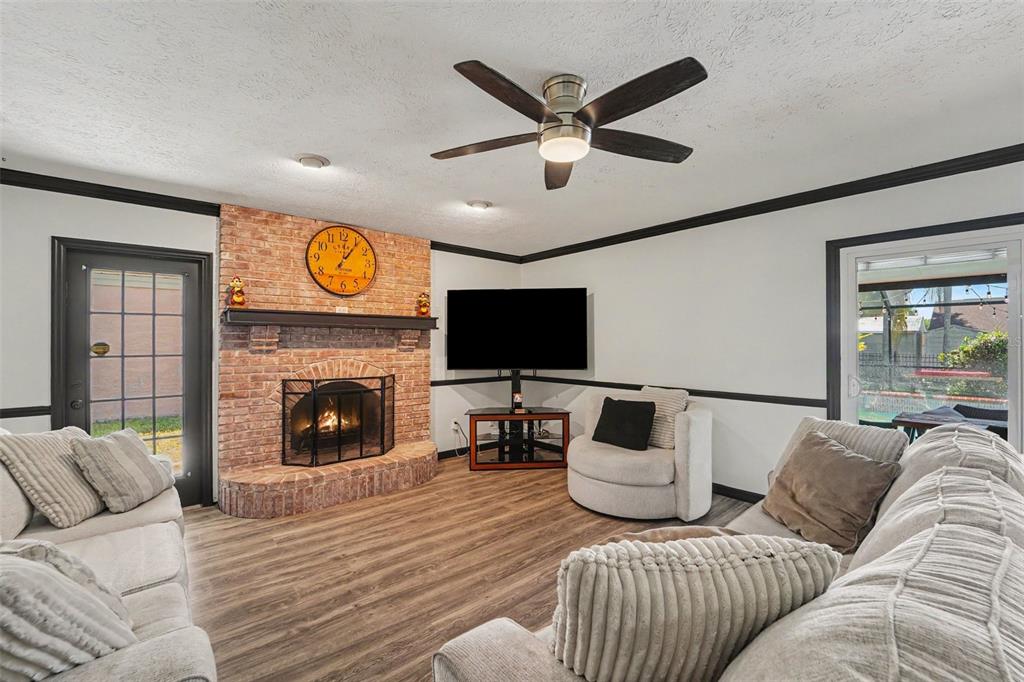 A living room features a brick fireplace, a ceiling fan, and light wood-look flooring — 717 CAMROSE DRIVE, BRANDON, FL