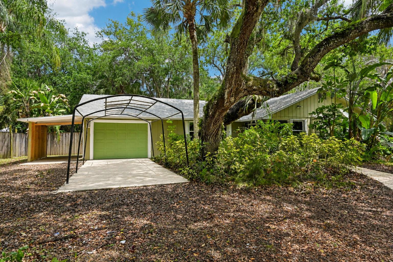A light green house with a garage, a metal carport, and a large oak tree — 255 SW Salerno Road, Stuart FL 34997, STUART, FL