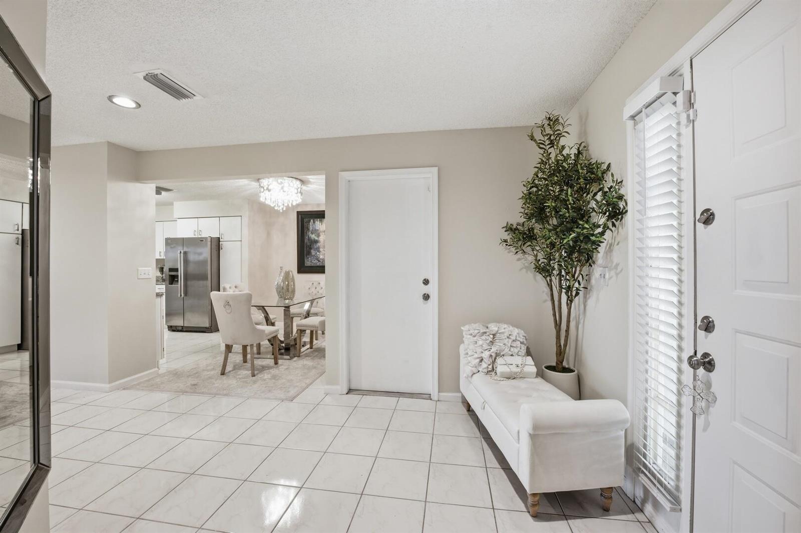 A bright entryway features white tile flooring, a white bench, a potted tree, and doors — 9172 Boca Gardens Parkway # B, Boca Raton FL 33496, BOCA RATON, FL
