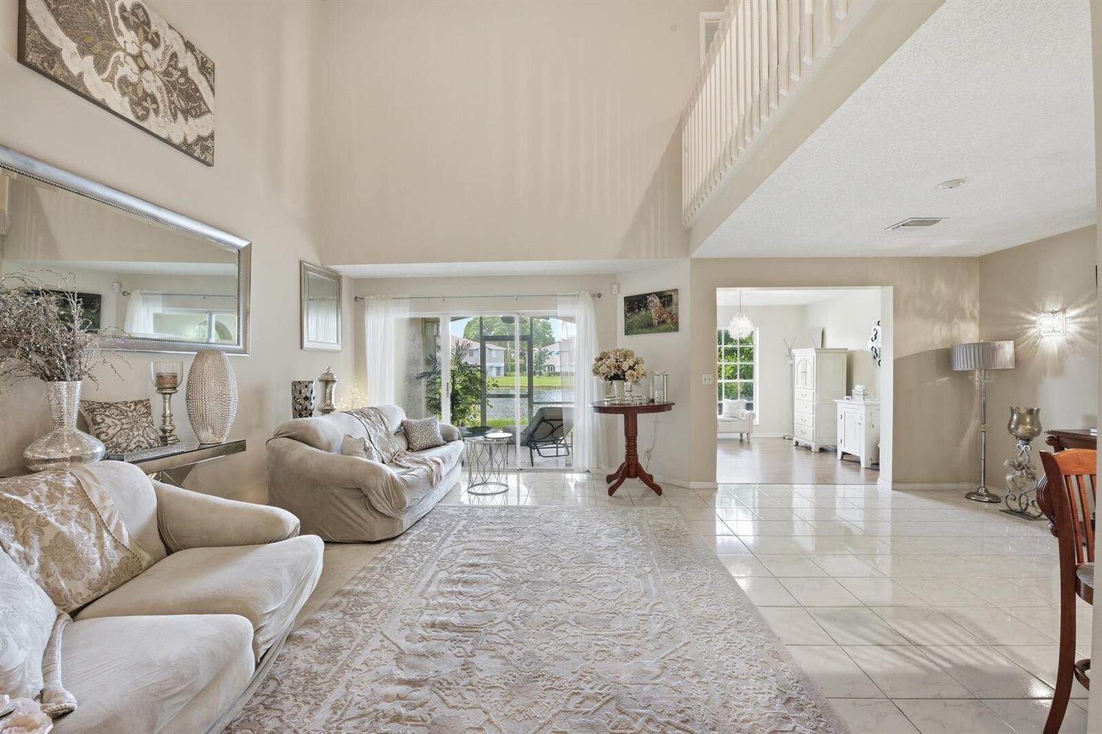 A bright living room features high ceilings, tile flooring, a large area rug, and patio access — 9172 Boca Gardens Parkway # B, Boca Raton FL 33496, BOCA RATON, FL