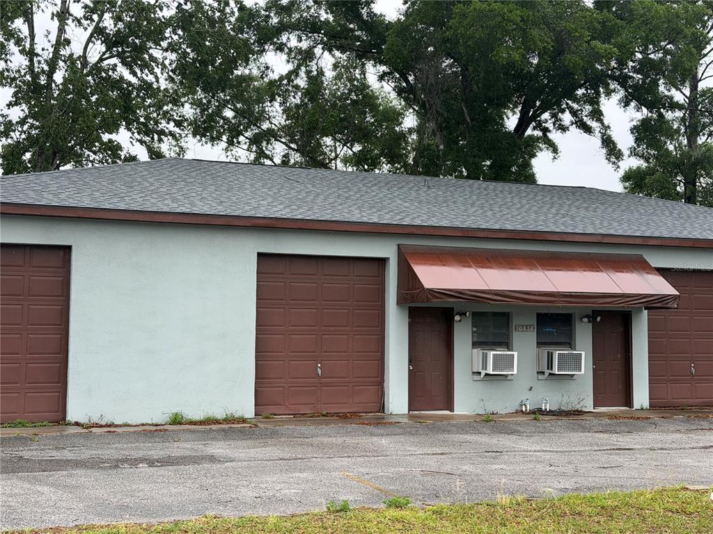 A single-story commercial building features light blue stucco walls, brown garage doors, and metal awnings — 10858 SW 91ST AVENUE, OCALA, FL
