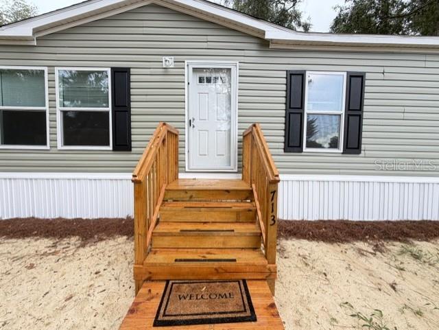The exterior of a manufactured home features light green siding, black shutters, and wooden stairs — 713 NE 3RD STREET, CHIEFLAND, FL