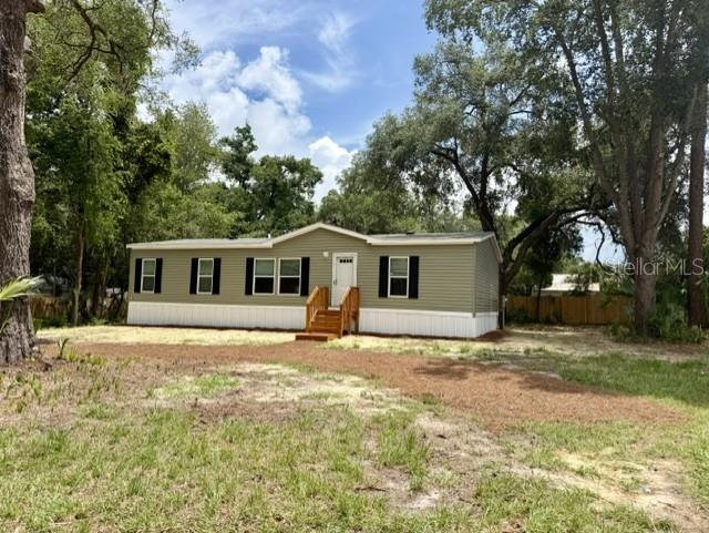 A light green manufactured home sits on a grassy lot surrounded by mature trees — 713 NE 3RD STREET, CHIEFLAND, FL