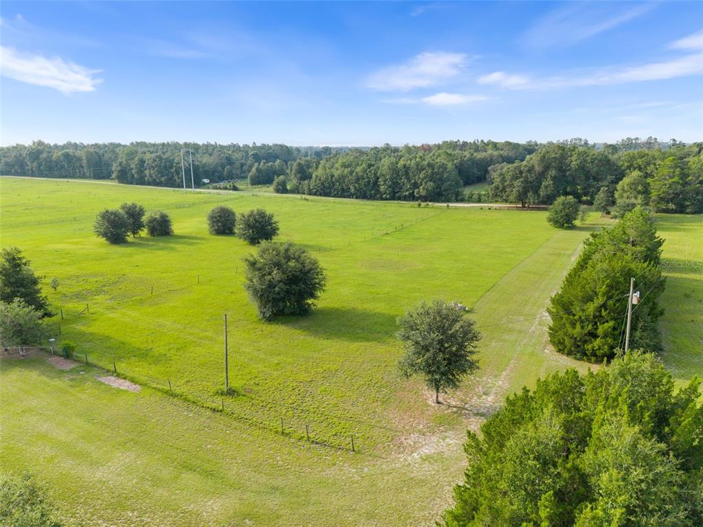 An aerial view shows a large, grassy pasture with scattered trees and a perimeter fence — 6690 SE 47TH PLACE, TRENTON, FL