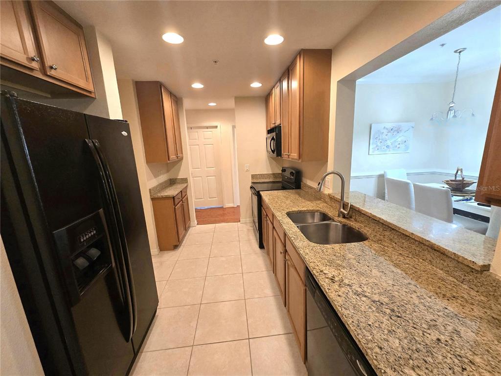 A galley kitchen features wood cabinets, granite countertops, stainless steel appliances, and tile flooring — 4005 OVERTURE CIRCLE UNIT 4005, BRADENTON, FL