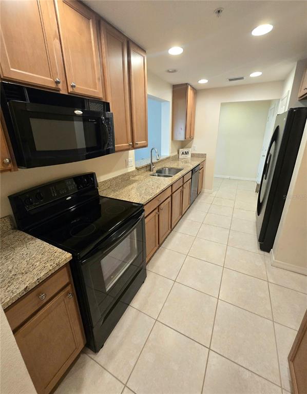 A kitchen features light wood cabinets, granite countertops, black appliances, and light tile flooring — 4005 OVERTURE CIRCLE UNIT 4005, BRADENTON, FL