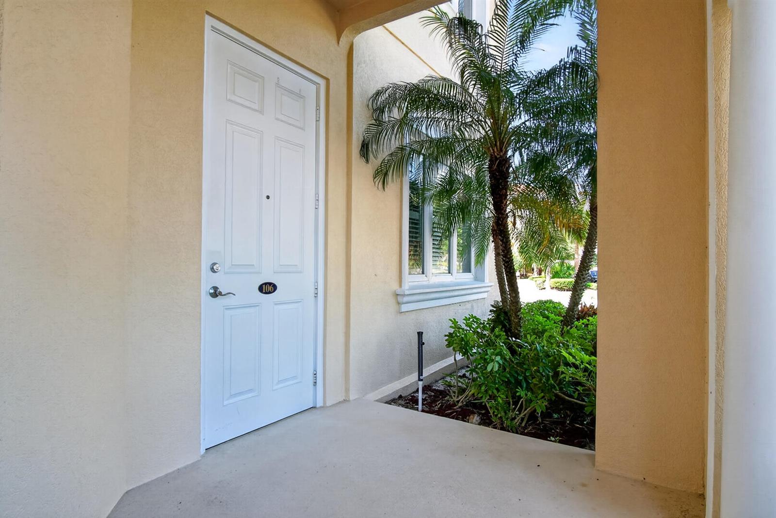 A white front door with the number 106 sits on a porch next to a palm tree — 37 E Harbour Isle Dr Drive E # 106, Fort Pierce FL 34949, FORT PIERCE, FL