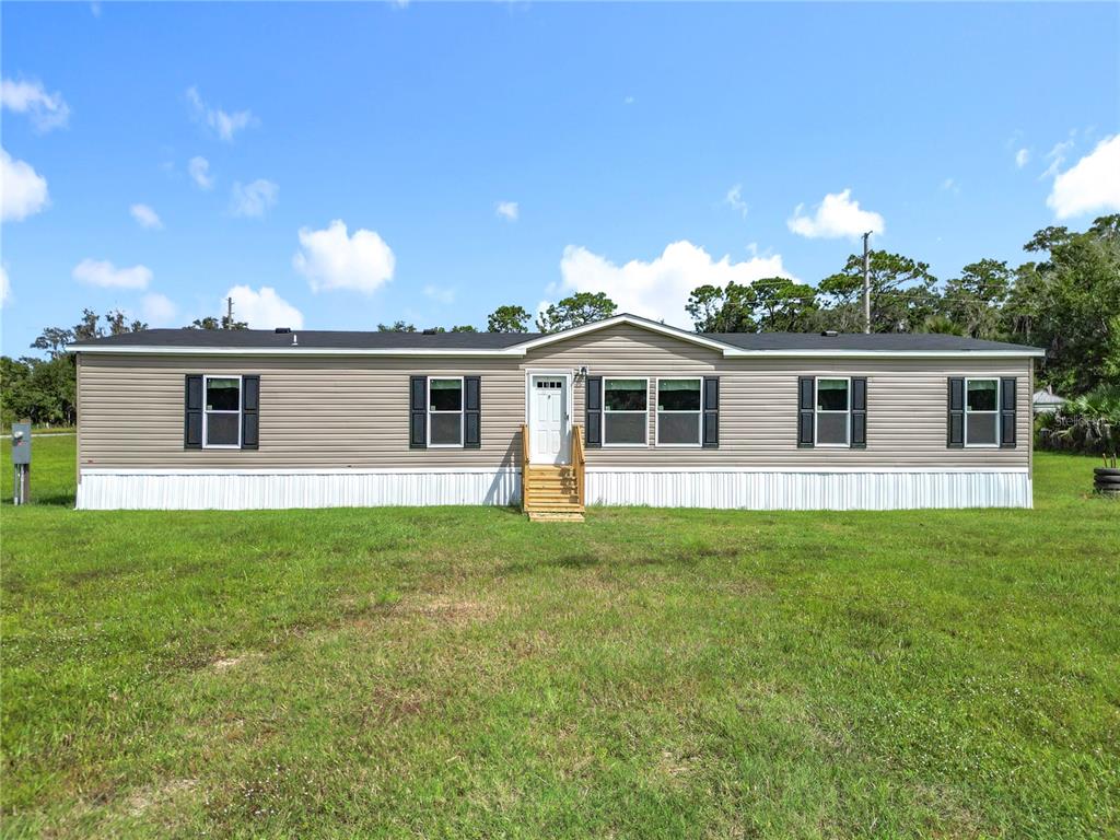 A single-story manufactured home with tan siding and a white skirt sits on a lawn — 8969 W CANDLEGLOW STREET, CRYSTAL RIVER, FL