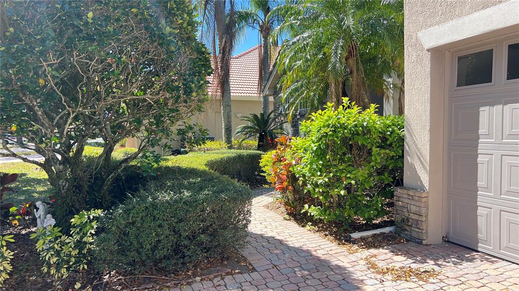 A brick walkway leads past lush landscaping toward the side of a house with a garage — 8854 OAK LANDINGS COURT, ORLANDO, FL
