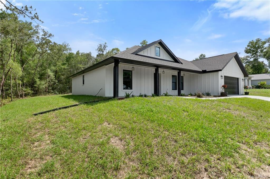 A modern white farmhouse with black trim and a dark roof sits on a grassy lot — 3058 E CROWN DRIVE, INVERNESS, FL