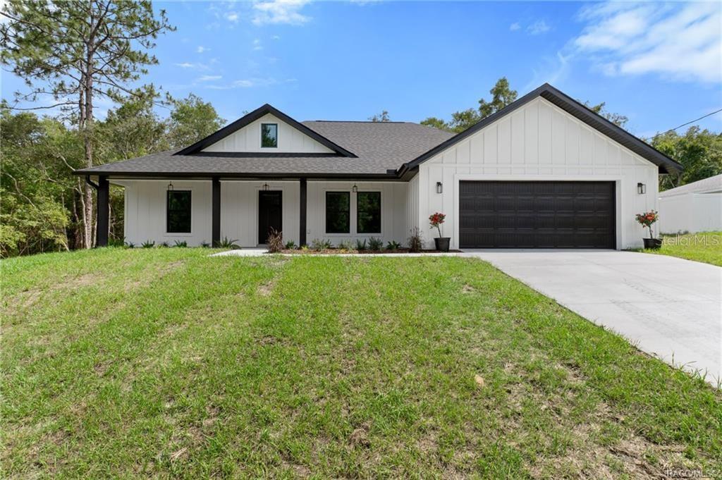 A modern single-story house with white vertical siding, a black roof, and a two-car garage — 3058 E CROWN DRIVE, INVERNESS, FL