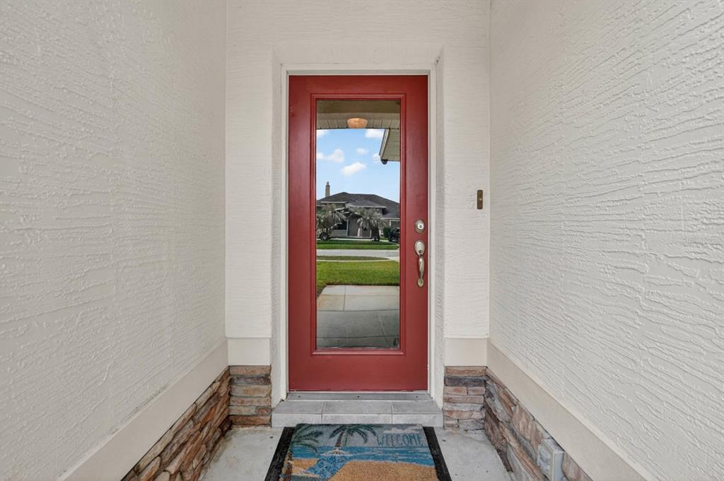 A red front door with a glass panel is set between textured walls and stone accents — 129 GREY DAPPLE WAY, ORMOND BEACH, FL