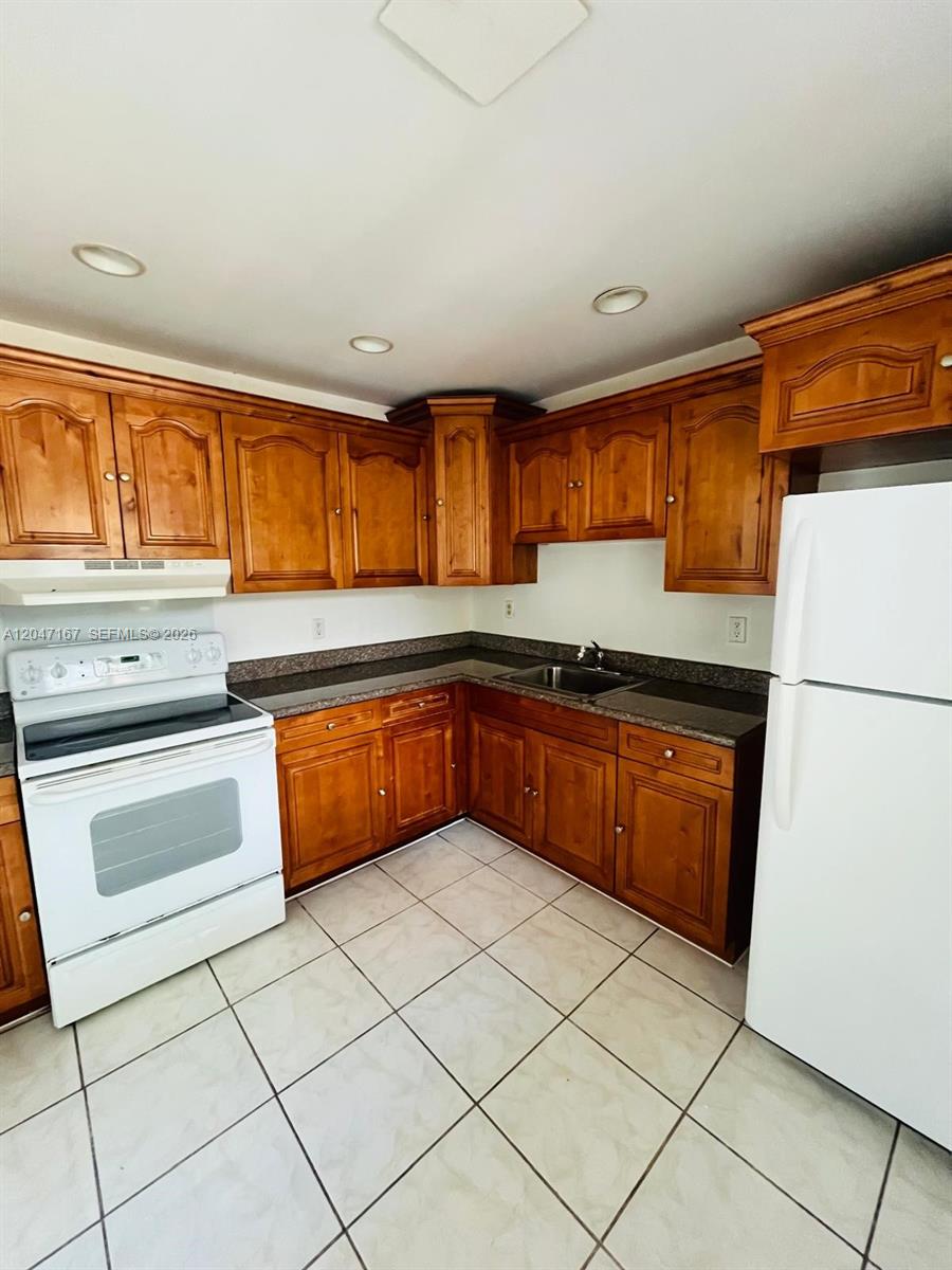 A kitchen features wood cabinets, dark countertops, a white stove, and a white refrigerator — 724 NE 4th St # 5, Hallandale Beach FL 33009, HALLANDALE BEACH, FL