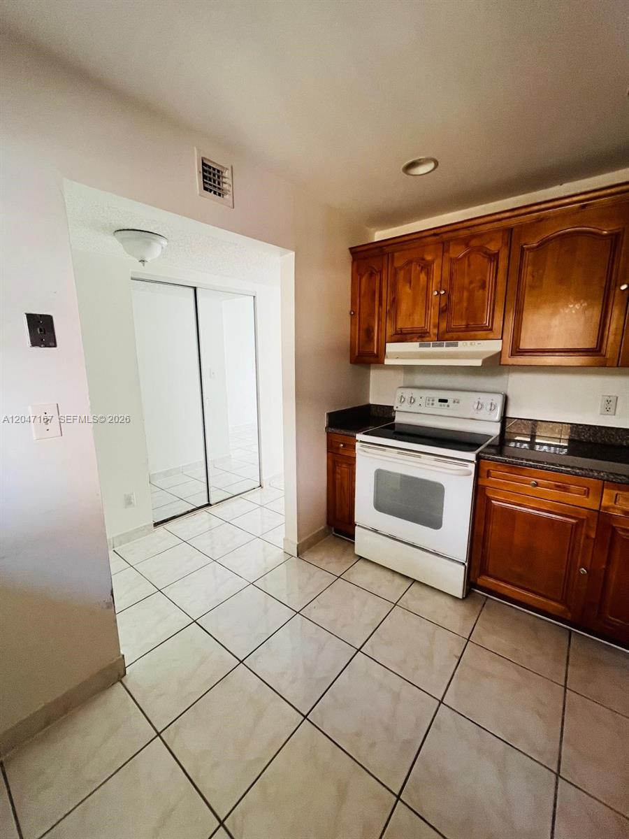 A kitchen features wooden cabinets, a white stove, and light-colored floor tiles — 724 NE 4th St # 5, Hallandale Beach FL 33009, HALLANDALE BEACH, FL