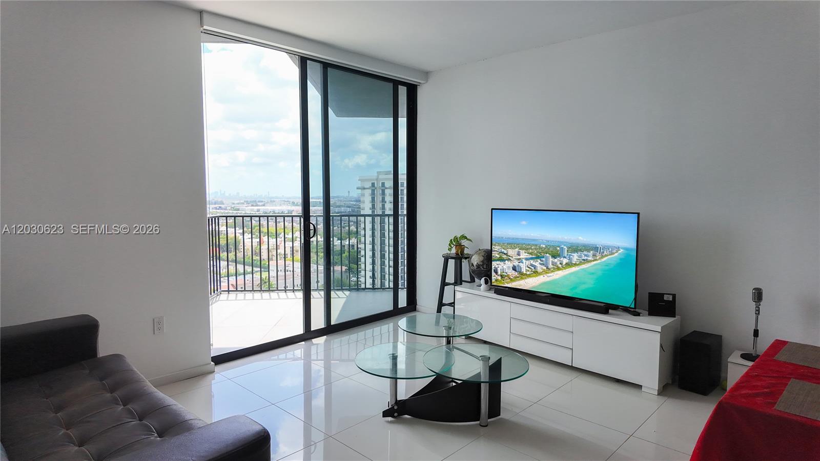 A living room features white tile floors, a glass coffee table, and a balcony view — 5300 Paseo Blvd # 1807, Doral FL 33166, DORAL, FL