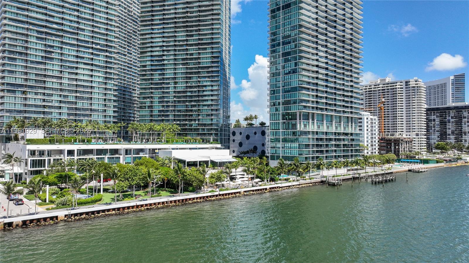 An aerial view shows high-rise residential towers along a waterfront with palm trees and landscaping — 480 NE 31st St # 1504, Miami FL 33137, MIAMI, FL