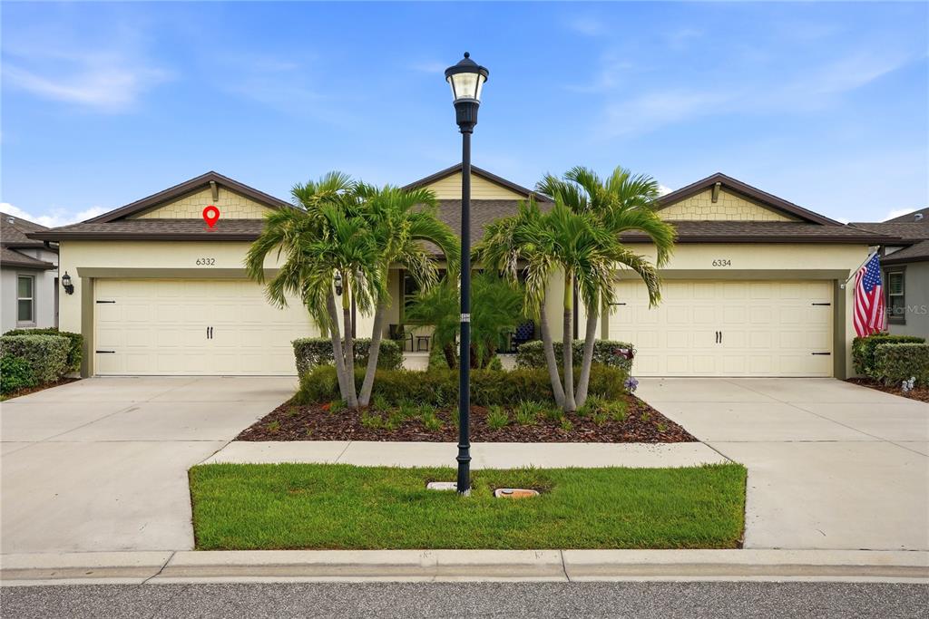 A duplex house exterior with two garage doors, palm trees, and a central street lamp — 6332 CLIVEDEN COURT, APOLLO BEACH, FL