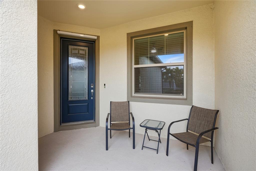 A covered entryway features a dark blue front door, a window, and two patio chairs — 6332 CLIVEDEN COURT, APOLLO BEACH, FL