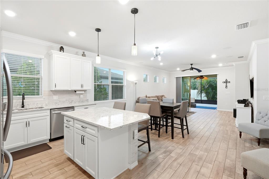 A kitchen with white cabinets and a granite island opens into a dining and living area — 6332 CLIVEDEN COURT, APOLLO BEACH, FL