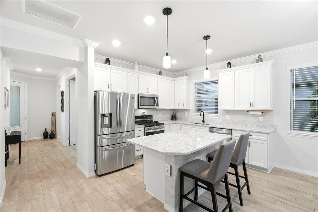 A bright kitchen features white cabinets, stainless steel appliances, a granite island, and wood-look flooring — 6332 CLIVEDEN COURT, APOLLO BEACH, FL