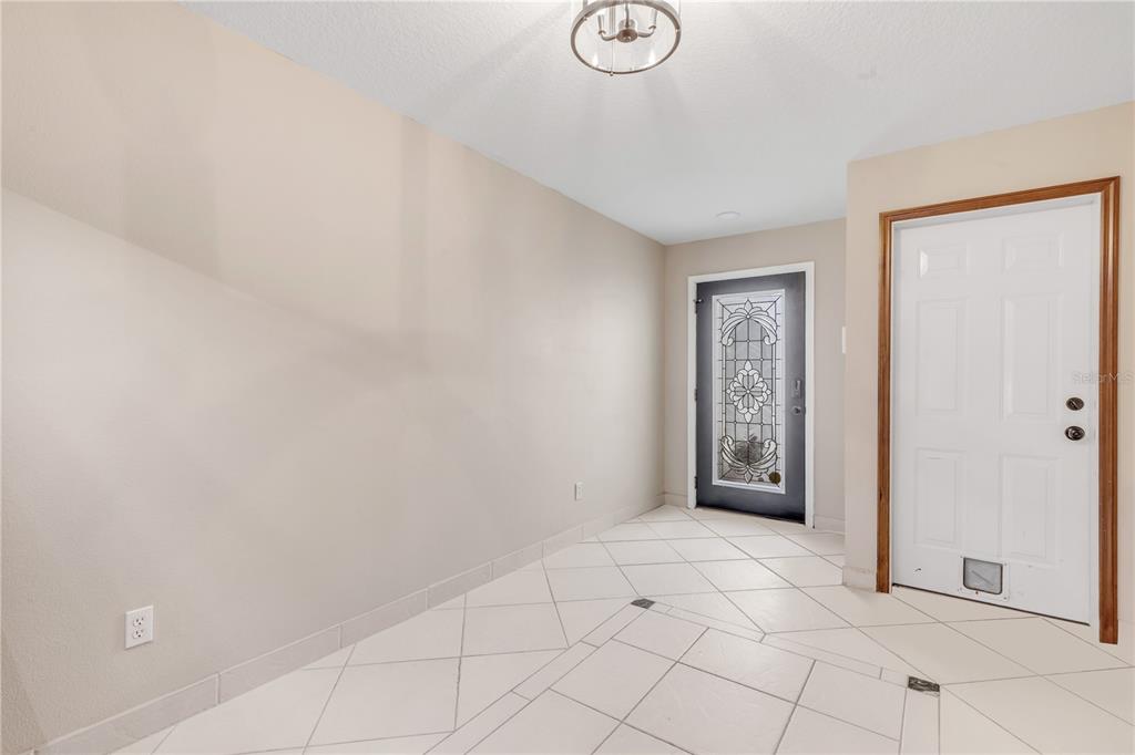 An entryway with white tiled floors, a large blank wall, and two exterior doors — 2236 DEERWOOD DRIVE, NEW SMYRNA BEACH, FL