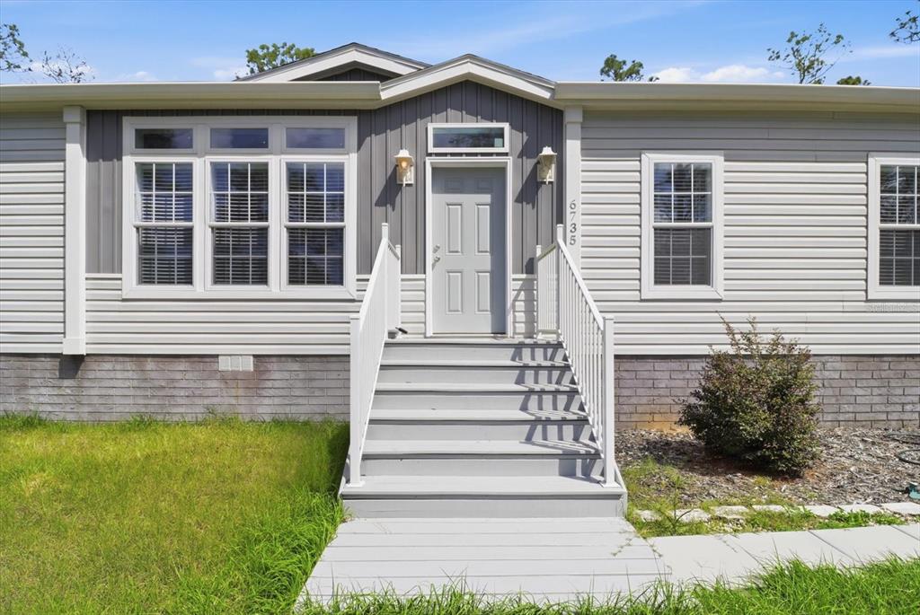 The exterior of a manufactured home features gray siding, a front staircase, and a doorway — 6735 W HOMOSASSA TRAIL, HOMOSASSA, FL