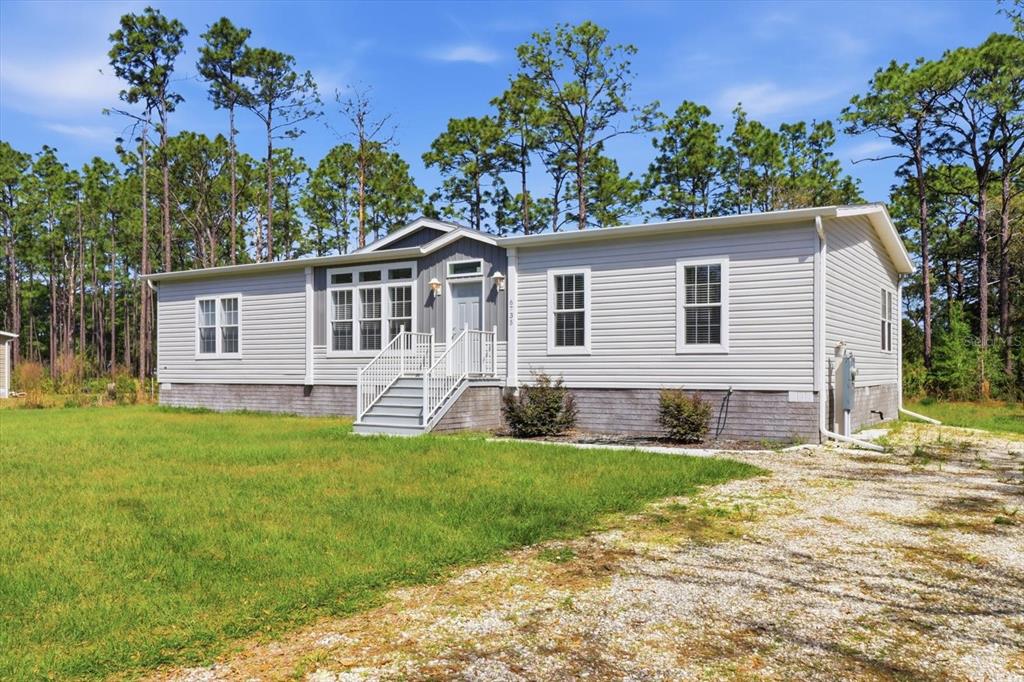 A single-story manufactured home with light gray siding sits on a gravel driveway — 6735 W HOMOSASSA TRAIL, HOMOSASSA, FL