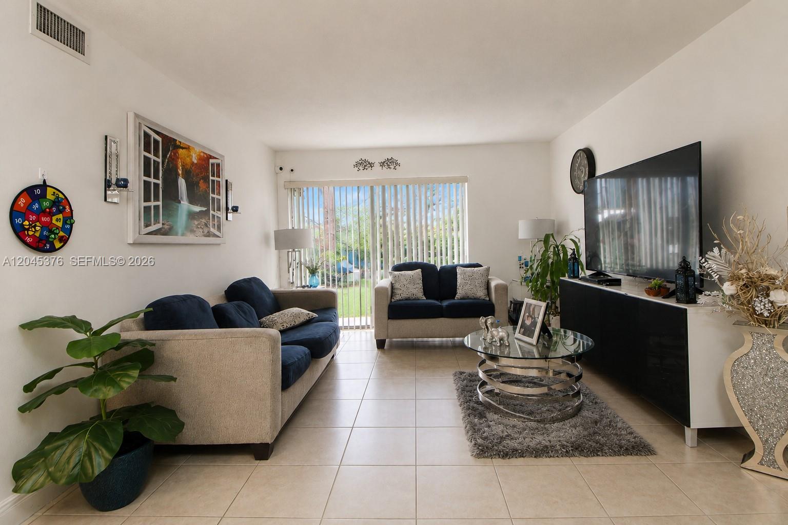 A living room features a blue sofa, a loveseat, a glass coffee table, and a television — 7090 NW 179th St # 108, Hialeah FL 33015, HIALEAH, FL