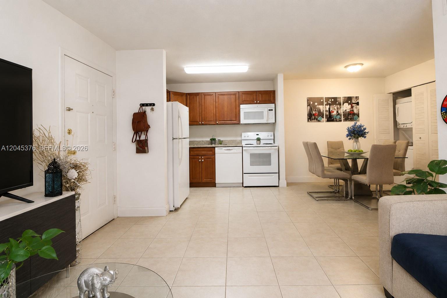 An open-concept kitchen and dining area features wood cabinets, white appliances, and tile flooring — 7090 NW 179th St # 108, Hialeah FL 33015, HIALEAH, FL