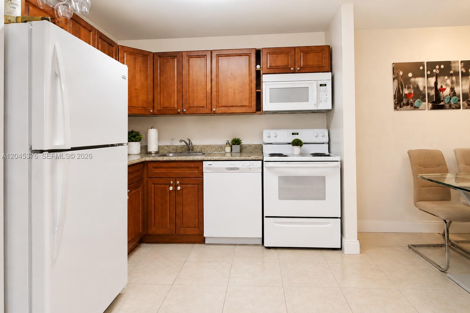 A kitchen features wood cabinets, white appliances, and light-colored tile flooring — 7090 NW 179th St # 108, Hialeah FL 33015, HIALEAH, FL